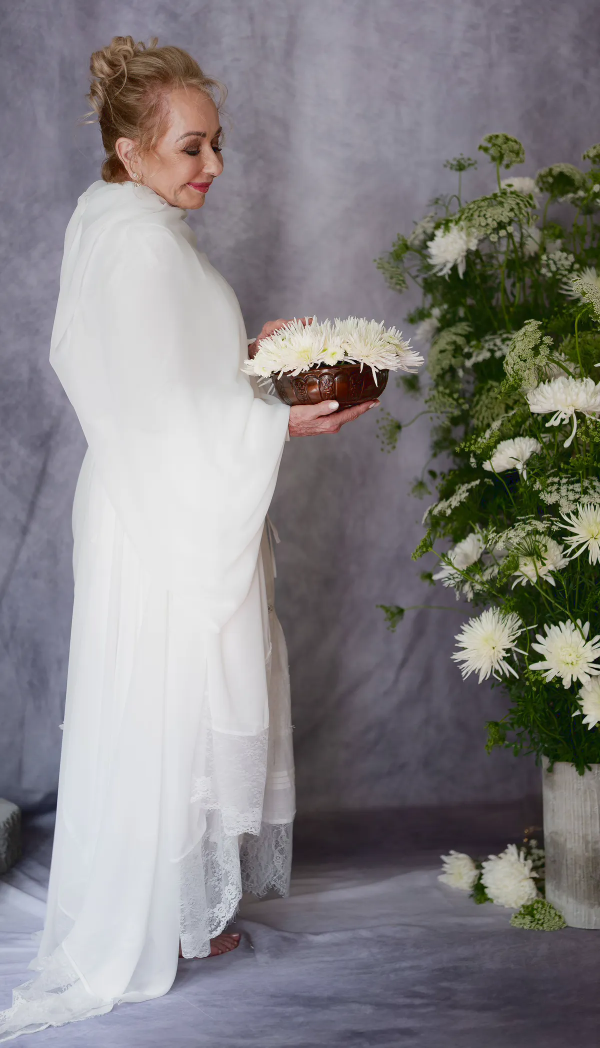 Candy, dressed in white, holding a bowl of white chrysanthemums.